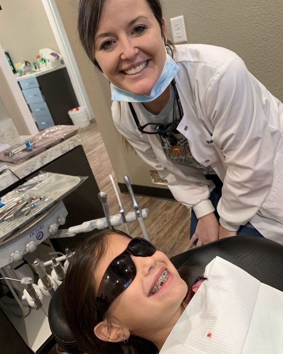 A young girl in sunglasses laughing in the dental chair beside her hygienist