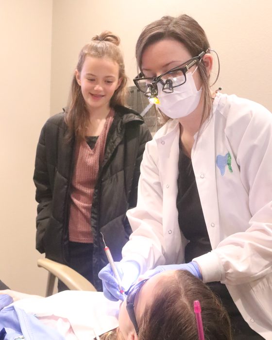 A hygienist treating a young patient while her mother stays close by