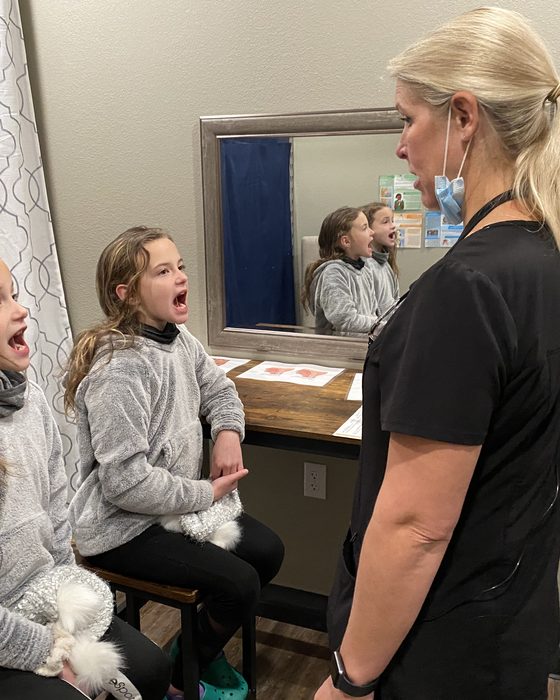 A myofunctional therapist coaching a young patient through tongue exercises at the mirror